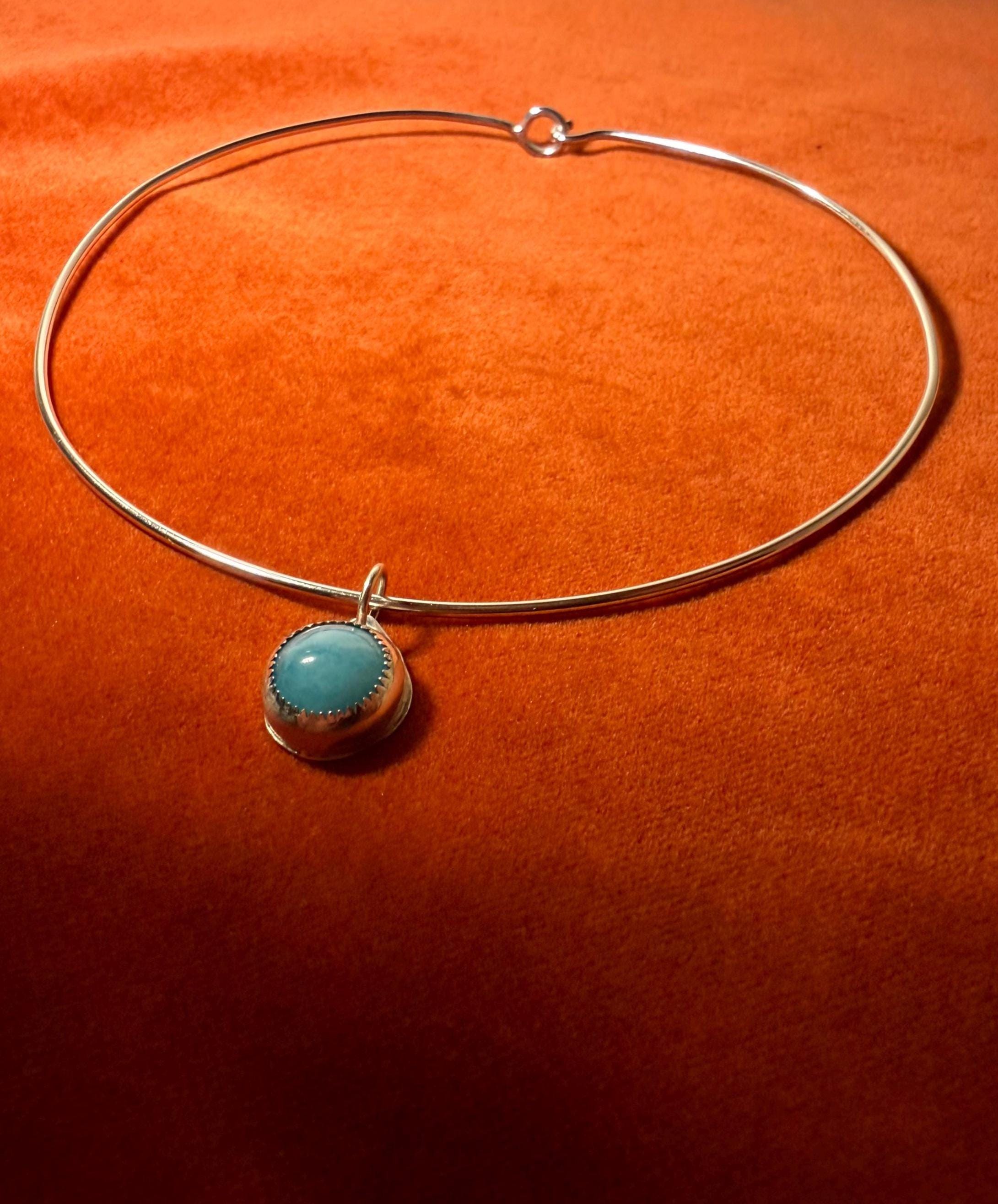Silver choker necklace with a blue-green stone pendant on an orange background.