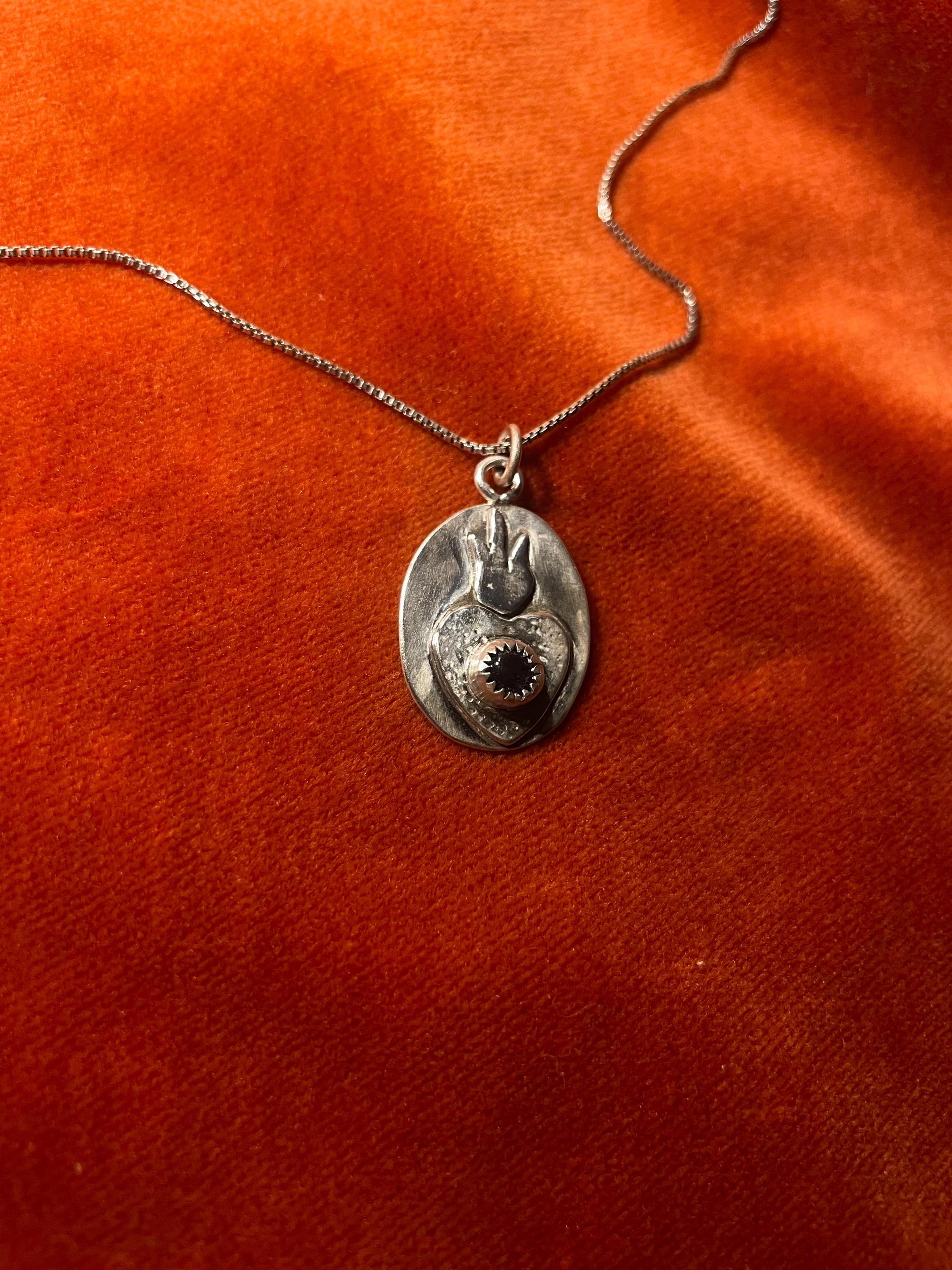 Silver chain with a sacred heart charm and an amethyst stone set in the center. Staged on an orange velvet background.