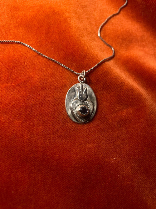 Silver chain with a sacred heart charm and an amethyst stone set in the center. Staged on an orange velvet background.