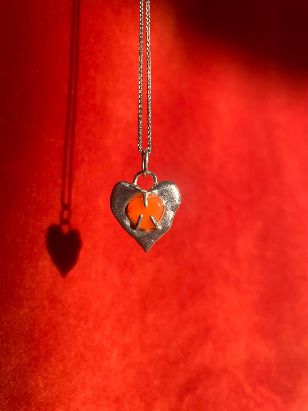 Heart-shaped pendant with a carnelian gemstone inset on a red background.