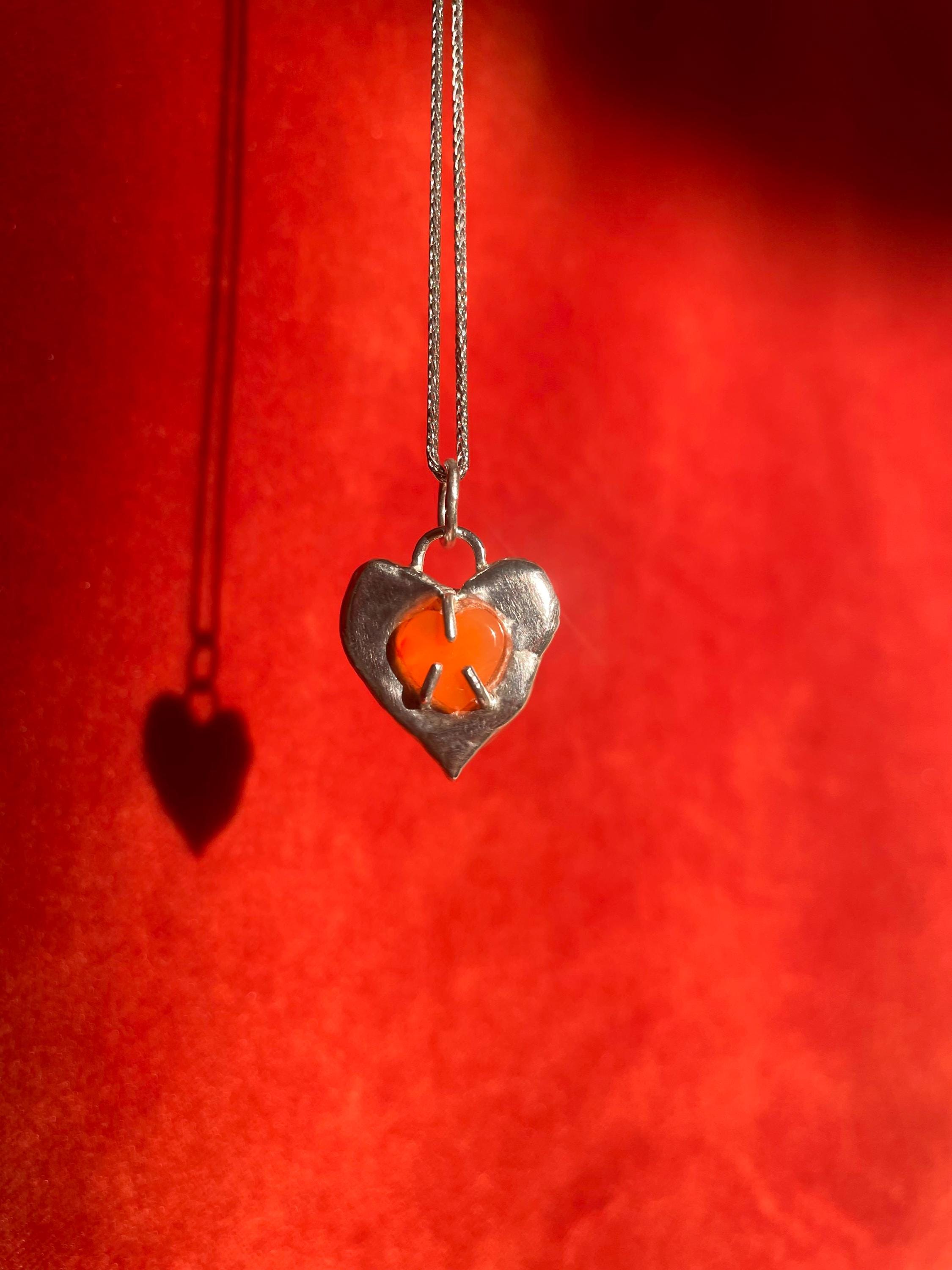 Heart-shaped pendant with a carnelian gemstone inset on a red background.