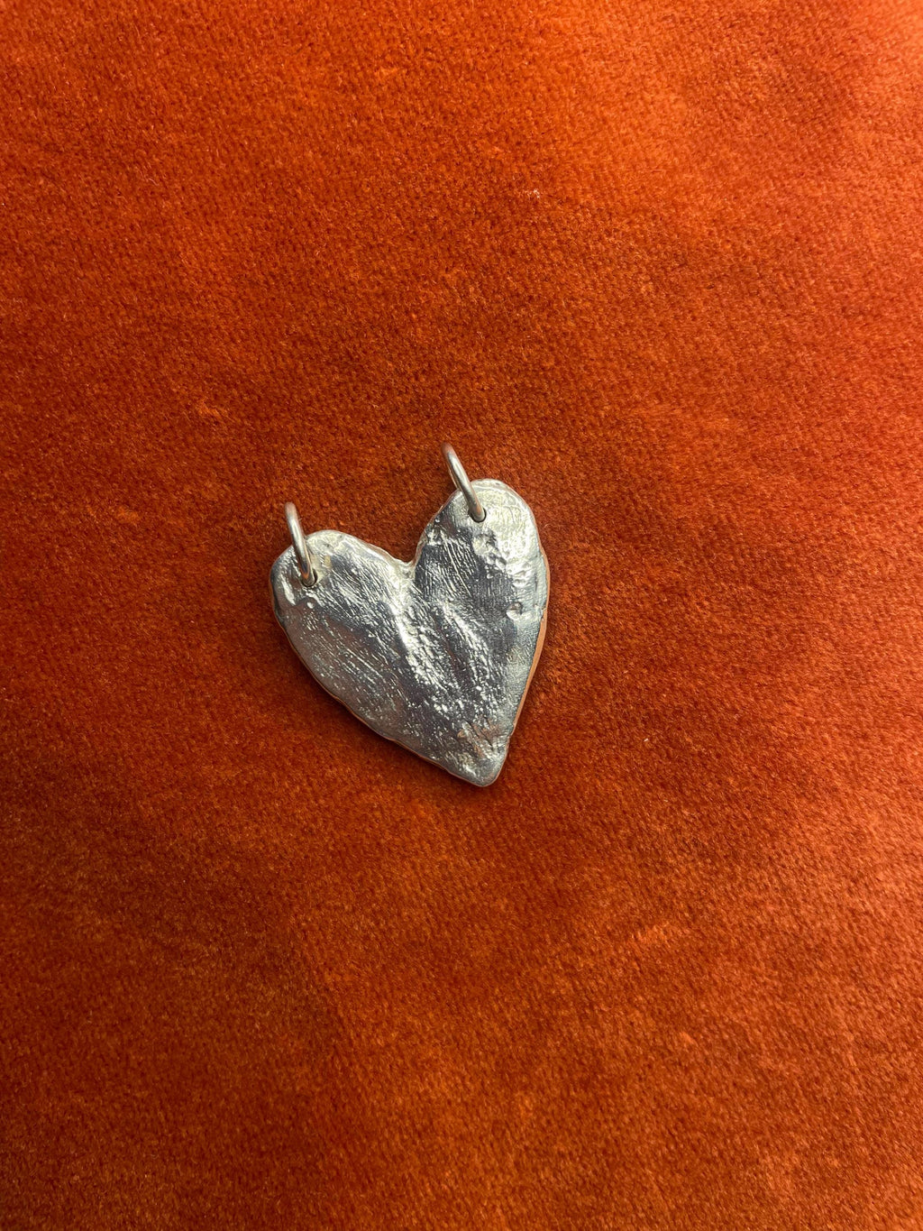 Silver heart-shaped pendant on a rust-colored fabric background.