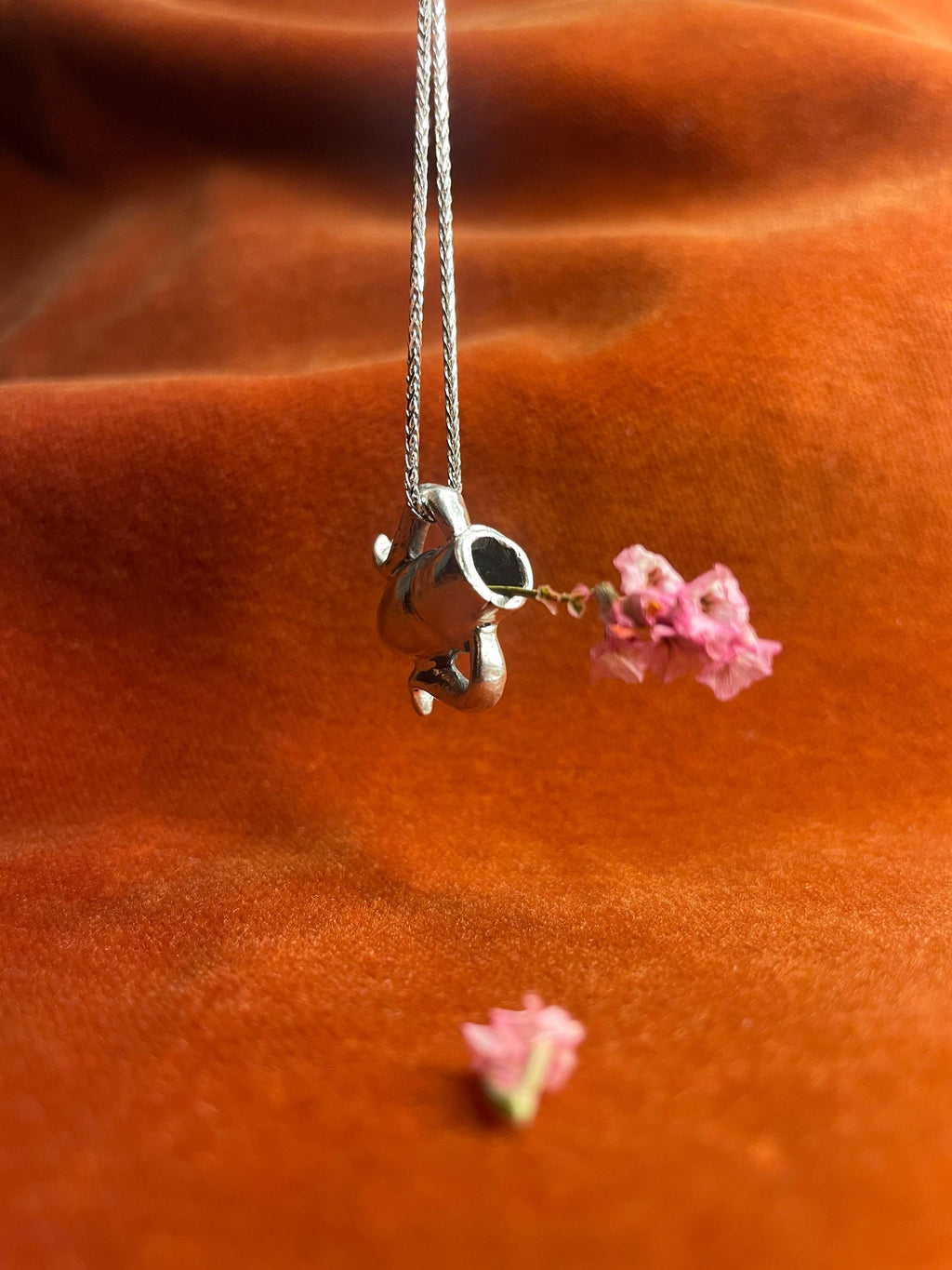 Silver chain with a vase charm and pink flowers on an orange fabric background.