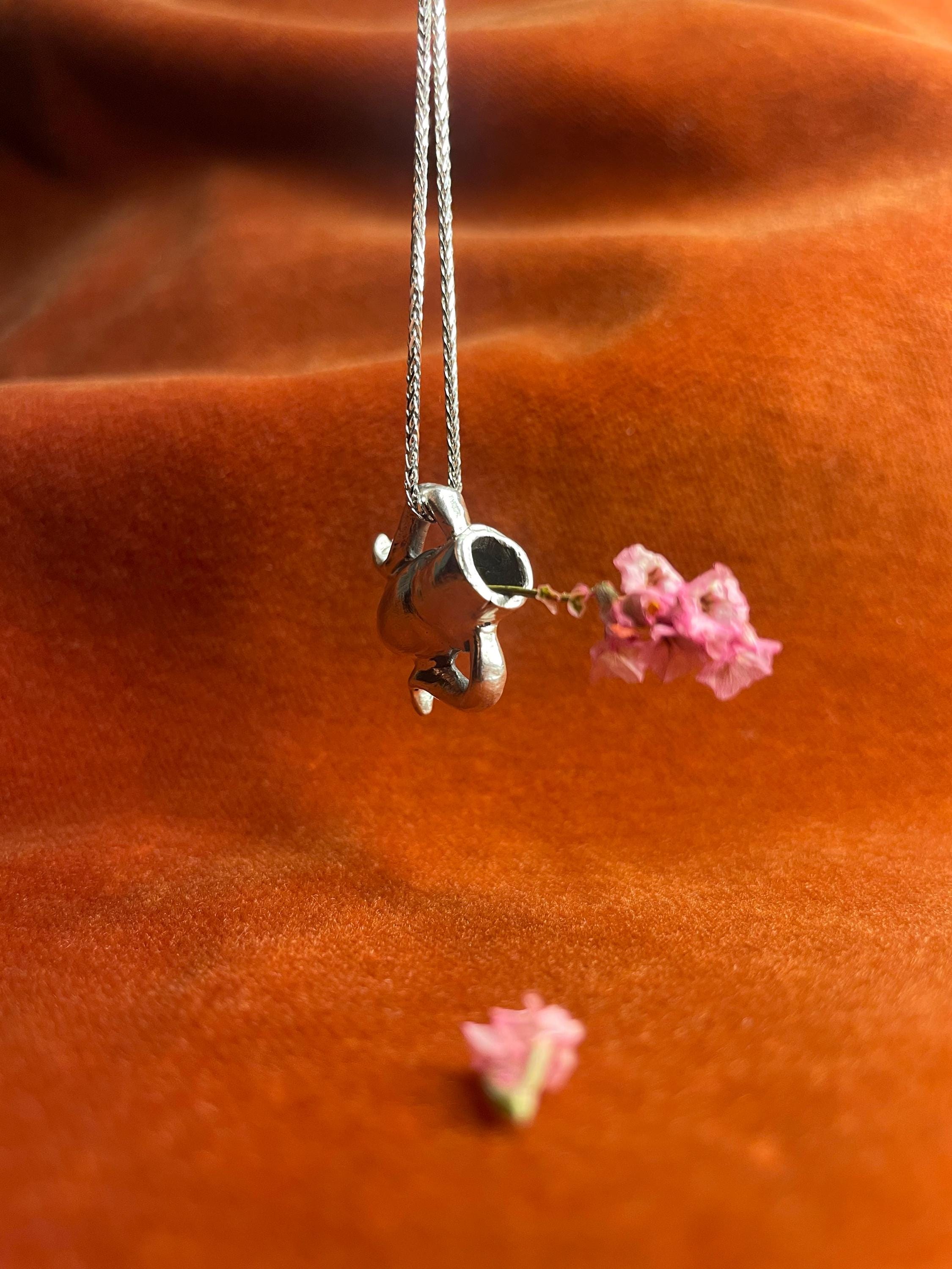 Silver chain with a vase charm and pink flowers on an orange fabric background.