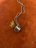 Silver chain with a small vase charm laying on an orange velvet surface.