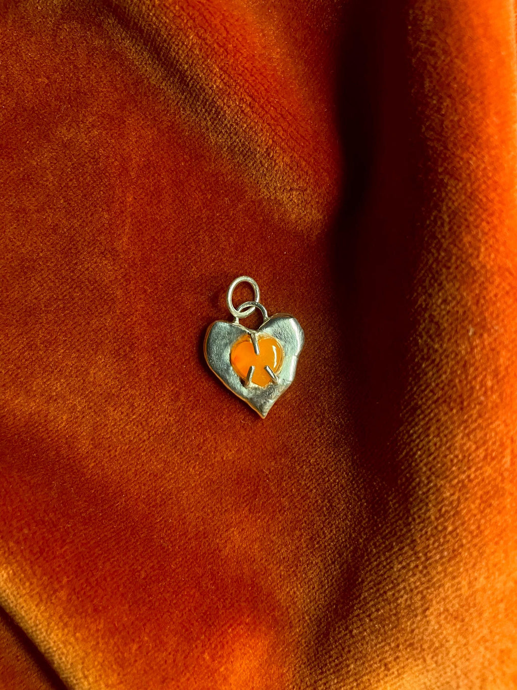 Heart-shaped charm with carnelian gemstone inset on an orange fabric background.