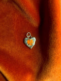 Heart-shaped charm with carnelian gemstone inset on an orange fabric background.