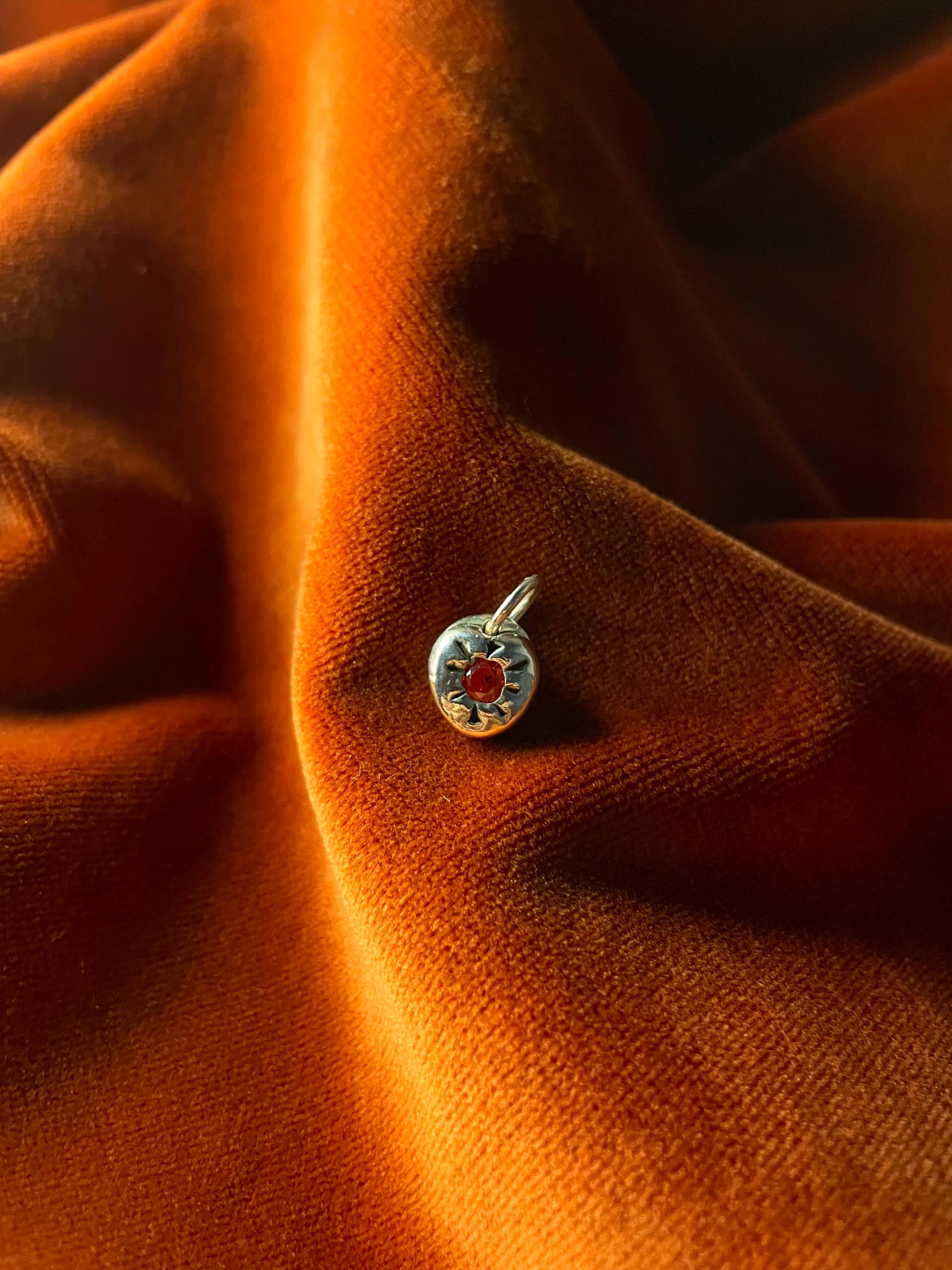 Silver charm with a red stone on orange fabric