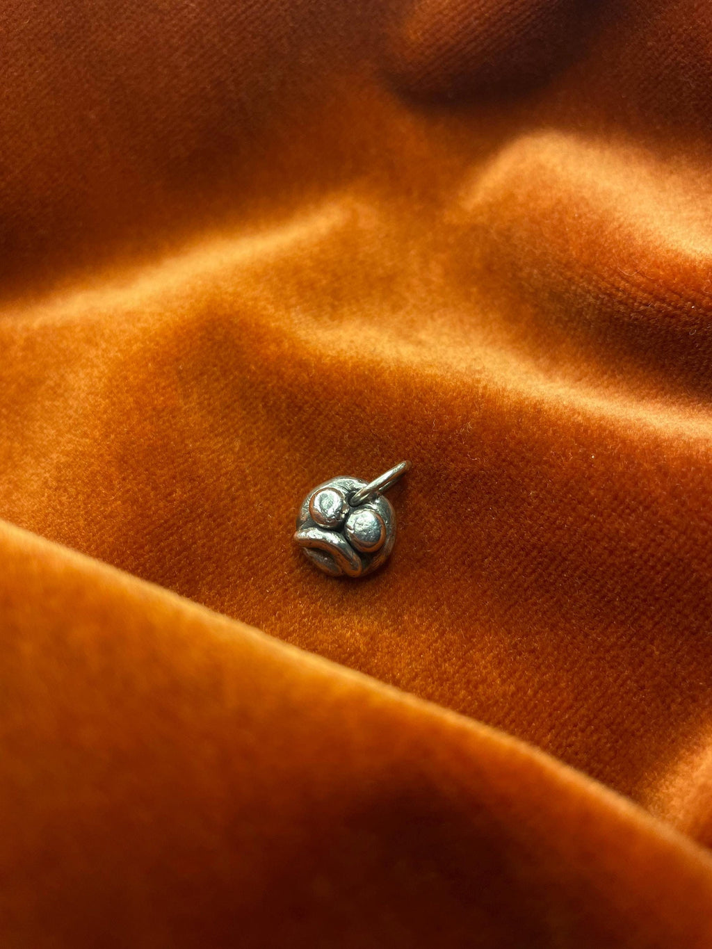 Silver frown face charm on orange fabric.