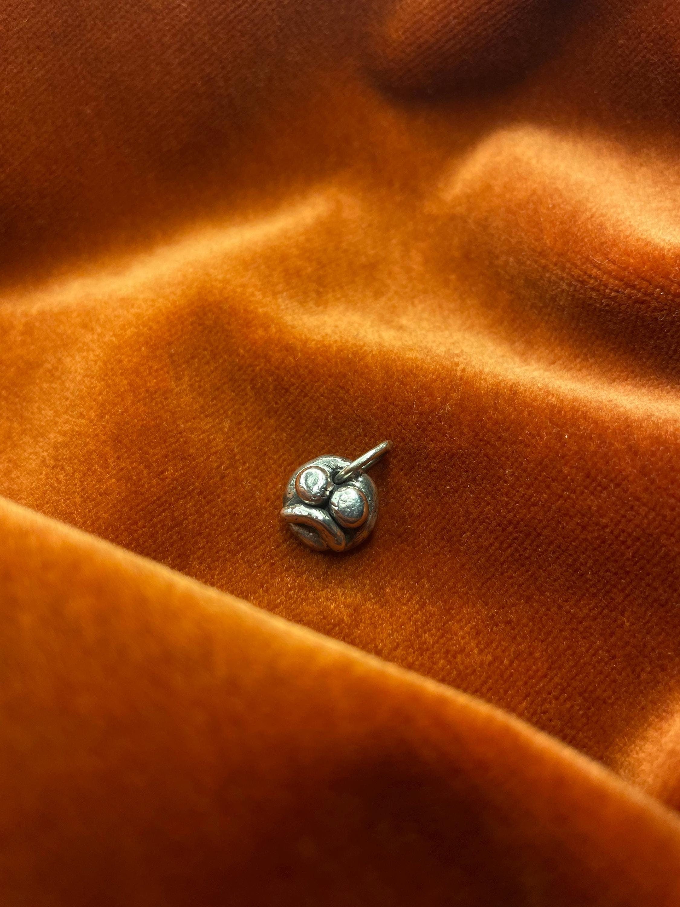 Silver frown face charm on orange fabric.