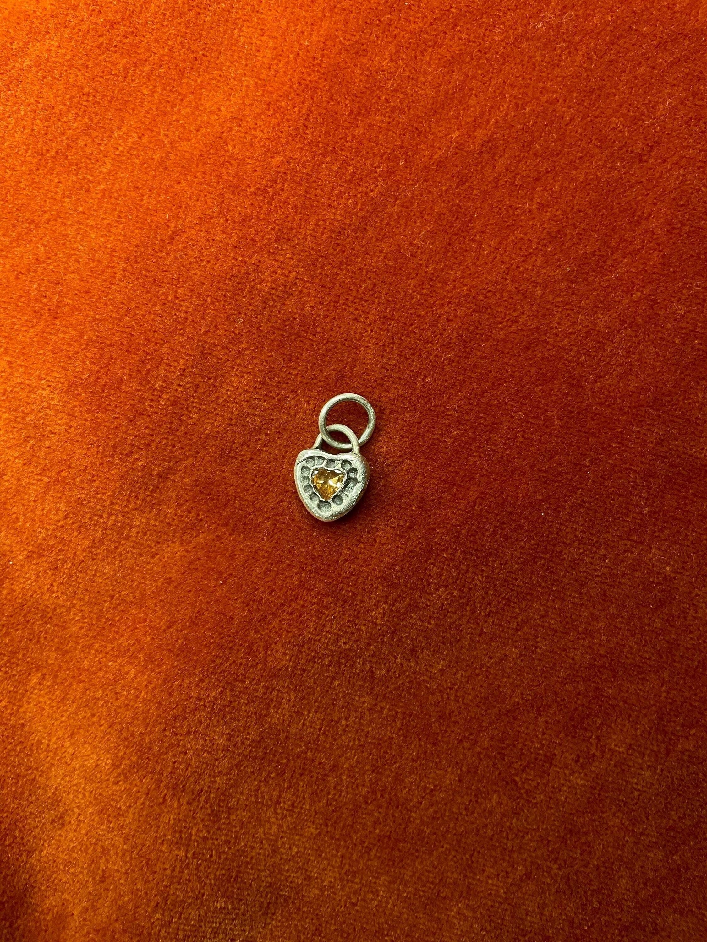 Heart-shaped charm with a yellow center on an orange fabric background.