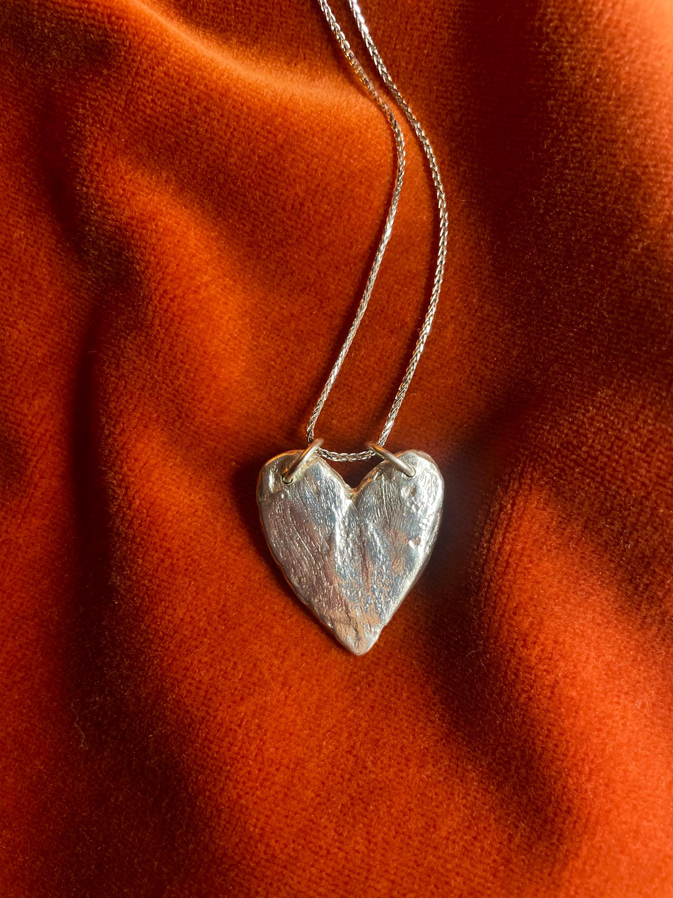 Silver heart-shaped pendant on a chain against an orange fabric background.