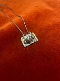 Silver necklace with a pendant of hands holding on an orange fabric background.