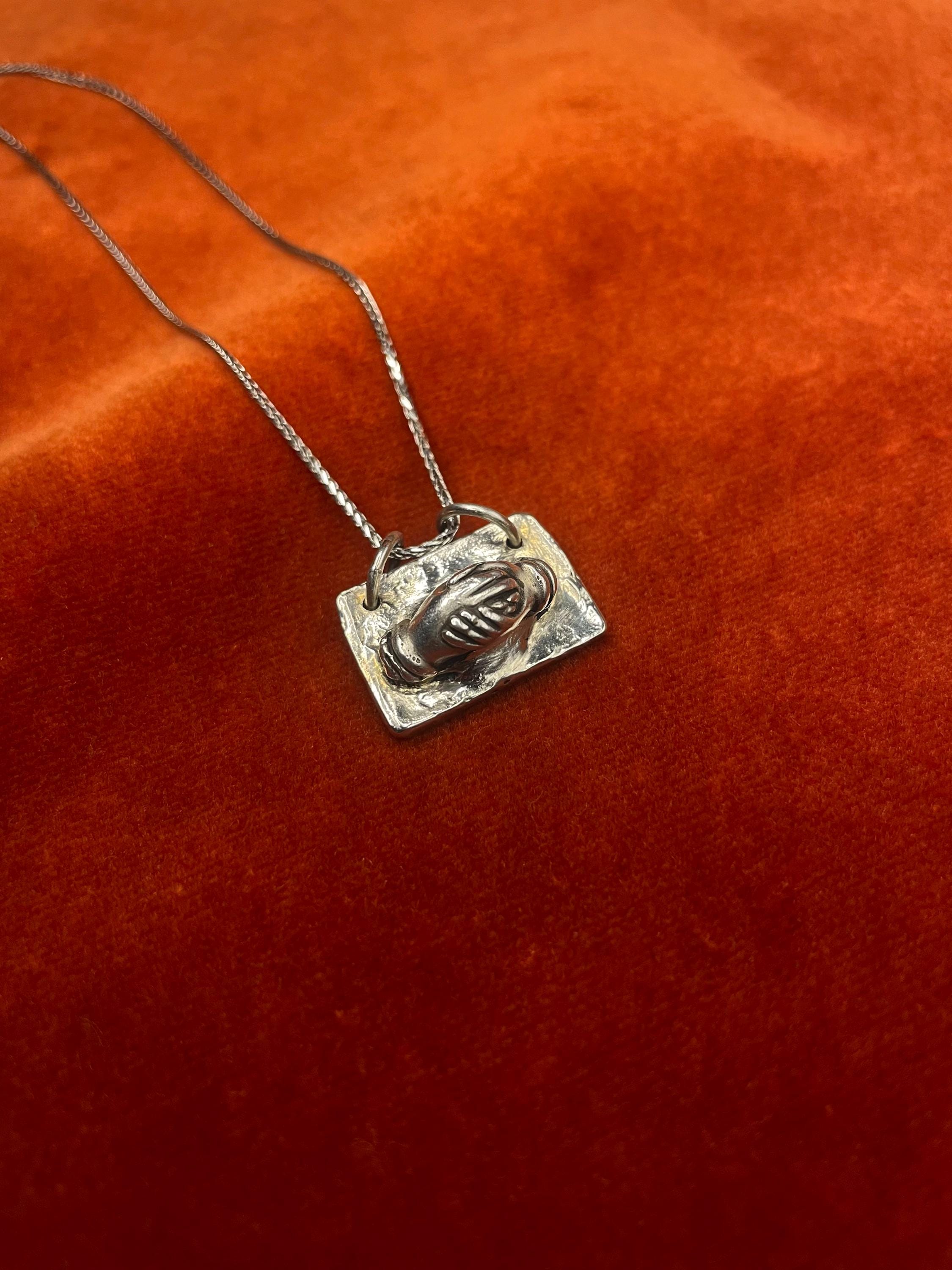 Silver necklace with a pendant of hands holding on an orange fabric background.
