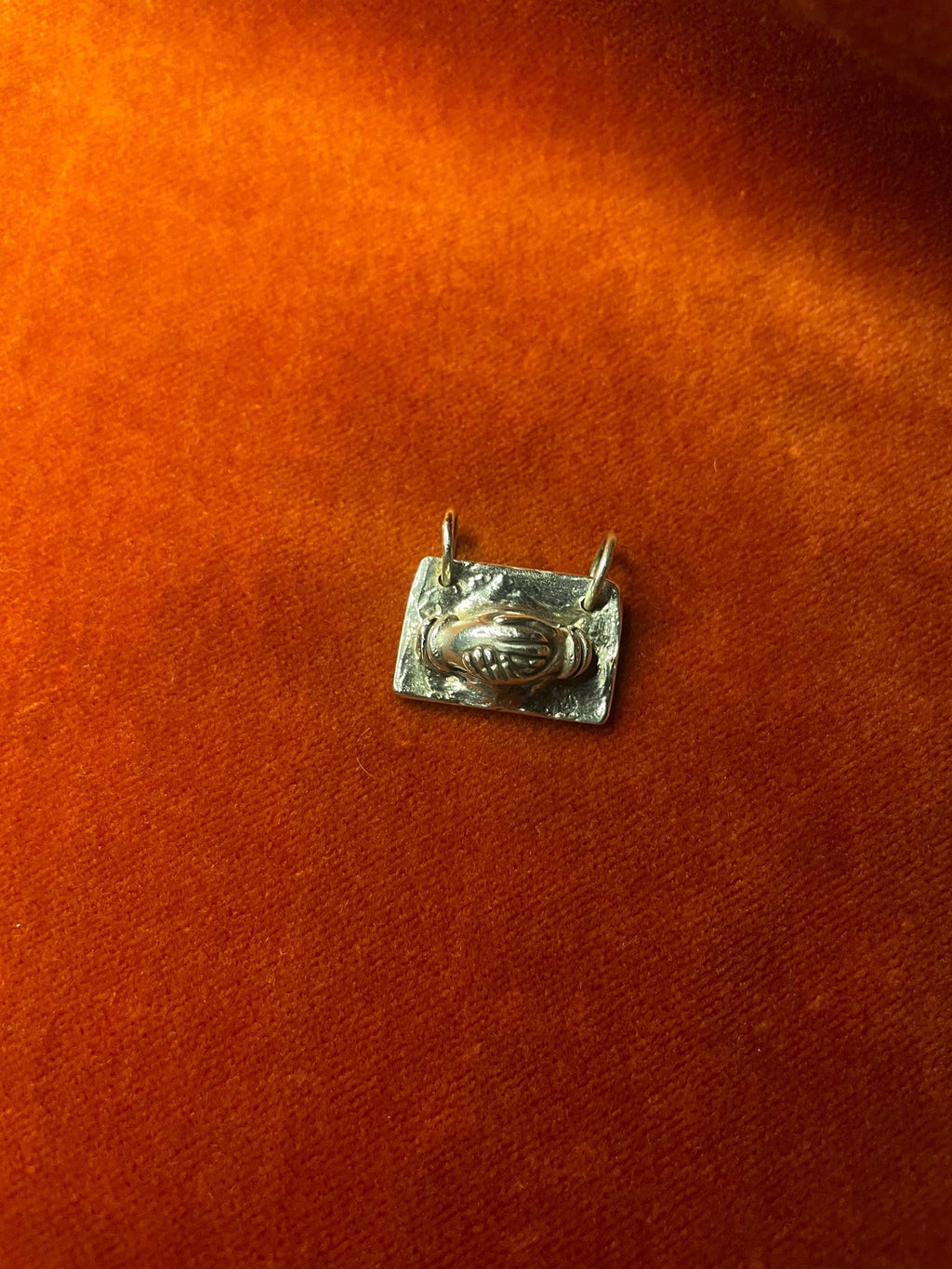 Silver holding hands pendant on a textured orange surface.