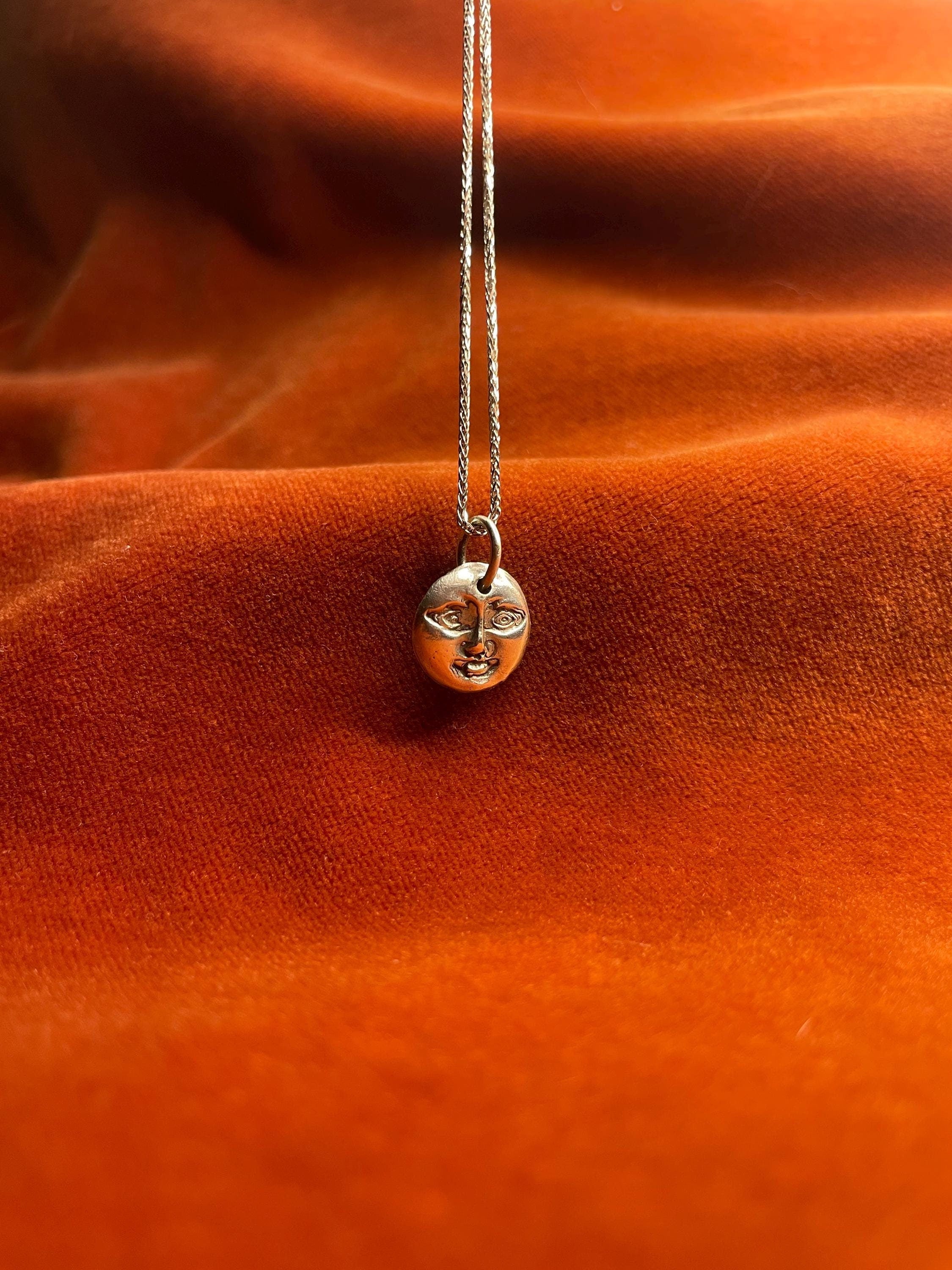 Silver necklace with a moon with a face charm on an orange fabric background.
