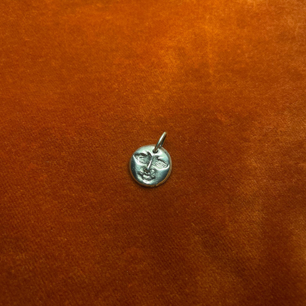 Silver moon face pendant on an orange surface.