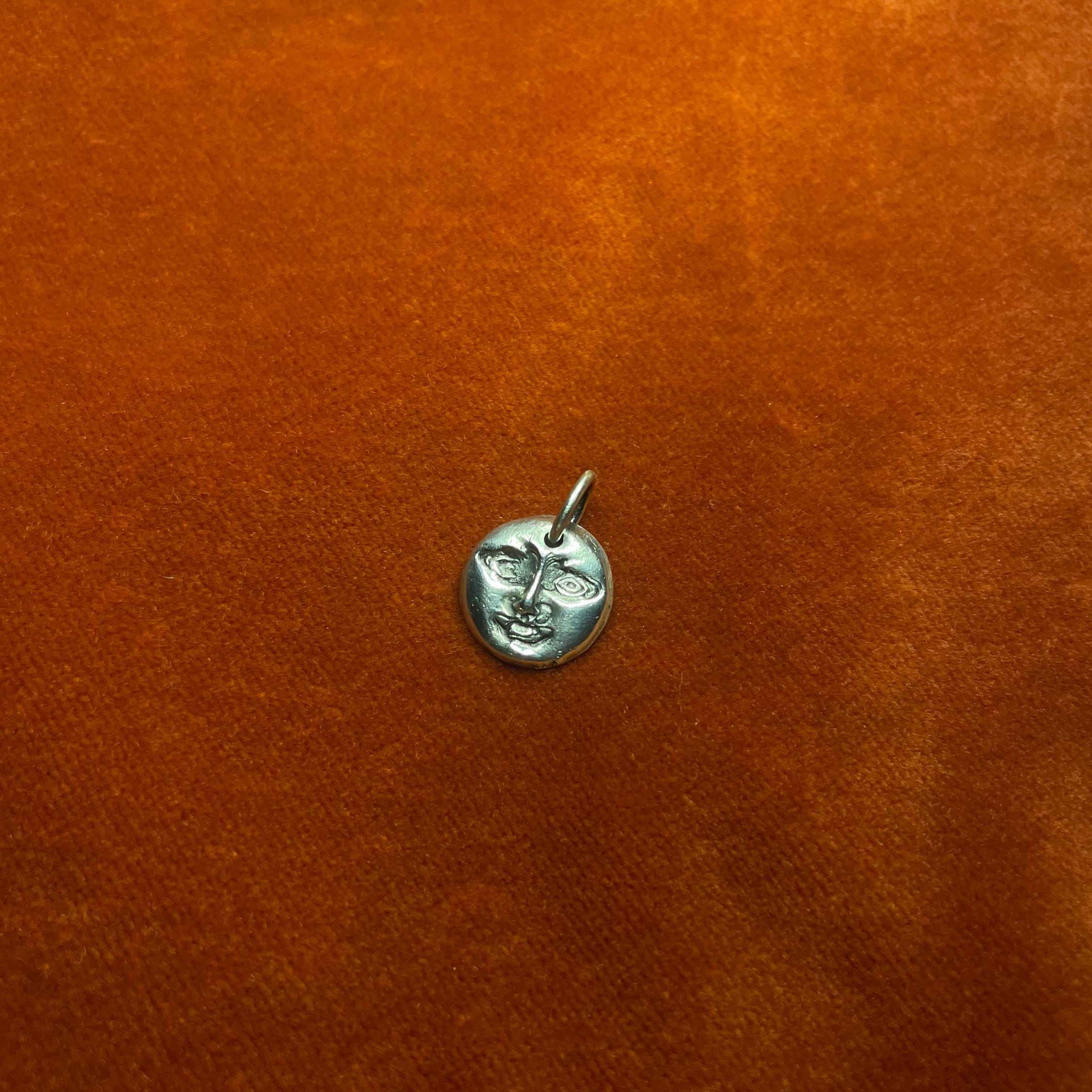 Silver moon face pendant on an orange surface.