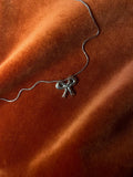 Silver bow-shaped charm on a silver chain laying against a orange fabric background.