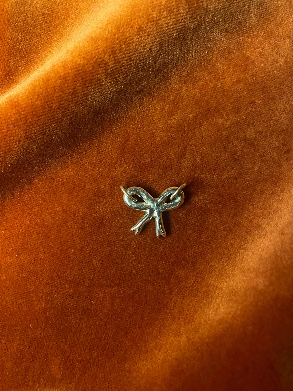 Silver bow-shaped charm on a orange fabric background.