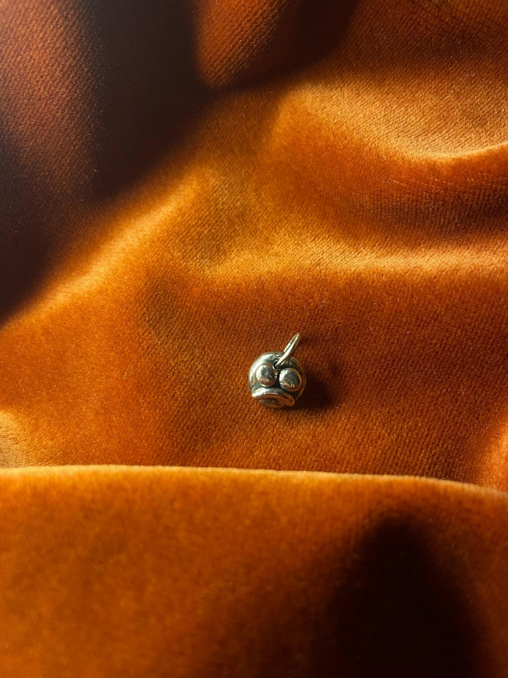 Close-up of a silver sad face charm on orange fabric.