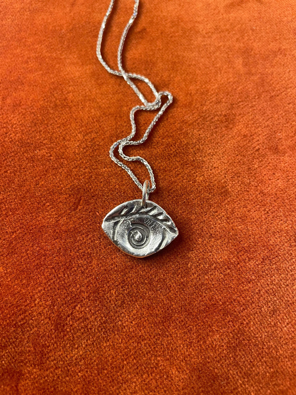 Silver chain with a spiral eye charm laying on an orange textured background.