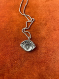 Silver chain with a spiral eye charm laying on an orange textured background.