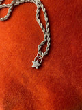 Silver chain with a star charm laying on an orange velvet background.