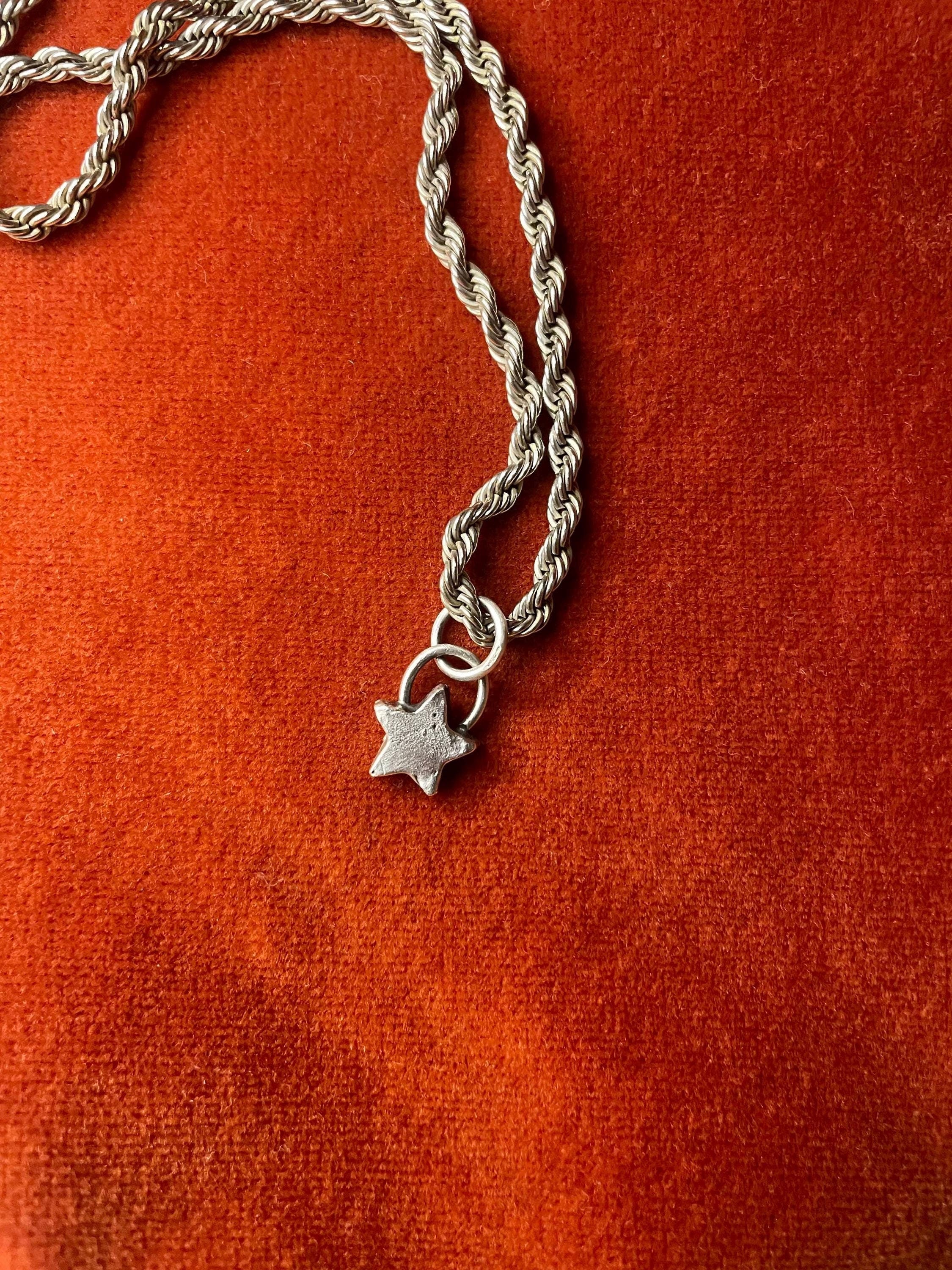 Silver chain with a star charm laying on an orange velvet background.