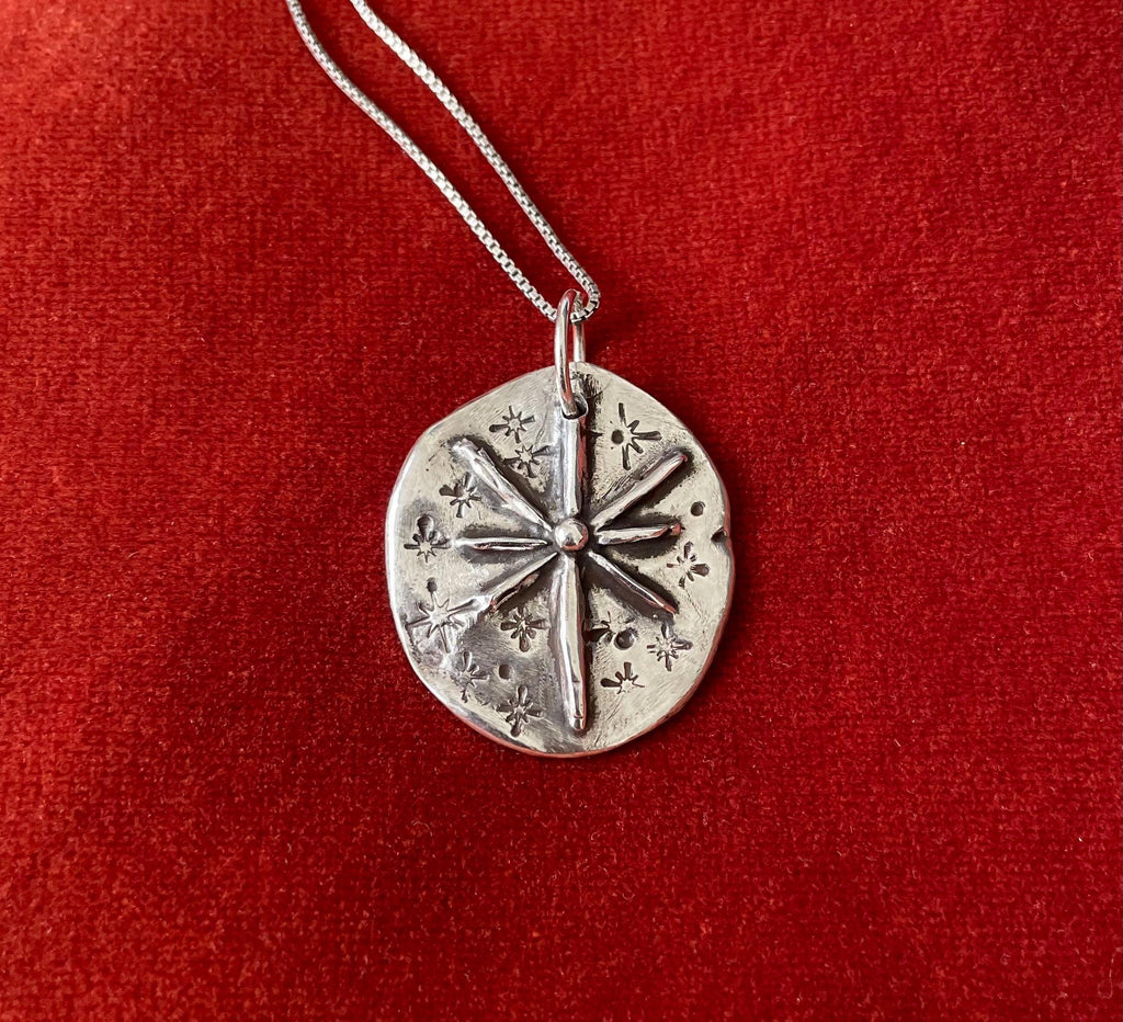 Silver charm necklace with a starburst charm laying on a red fabric background.