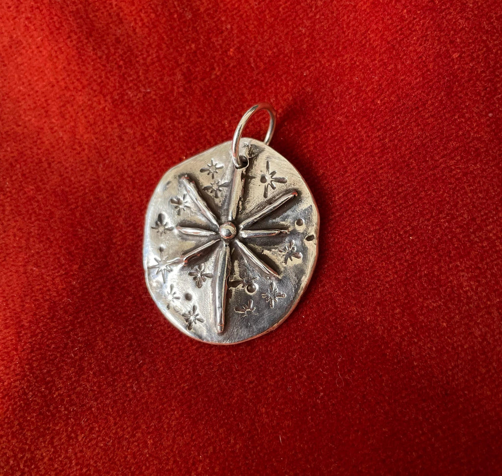 Silver charm with star burst design laying on a red background.