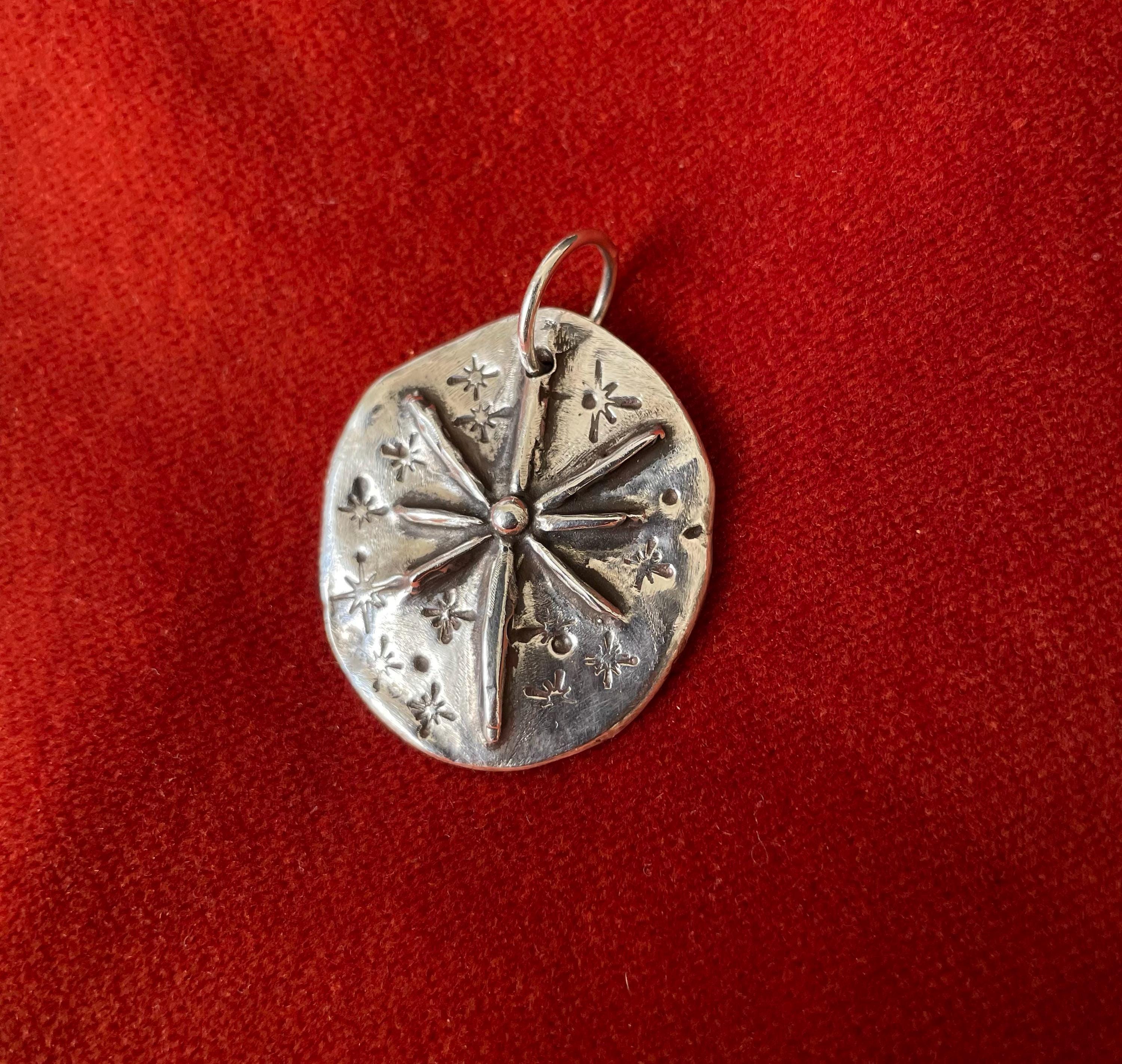 Silver charm with star burst design laying on a red background.