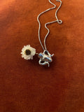 Silver chain with a white flower inside of a vase charm laying on an orange surface.