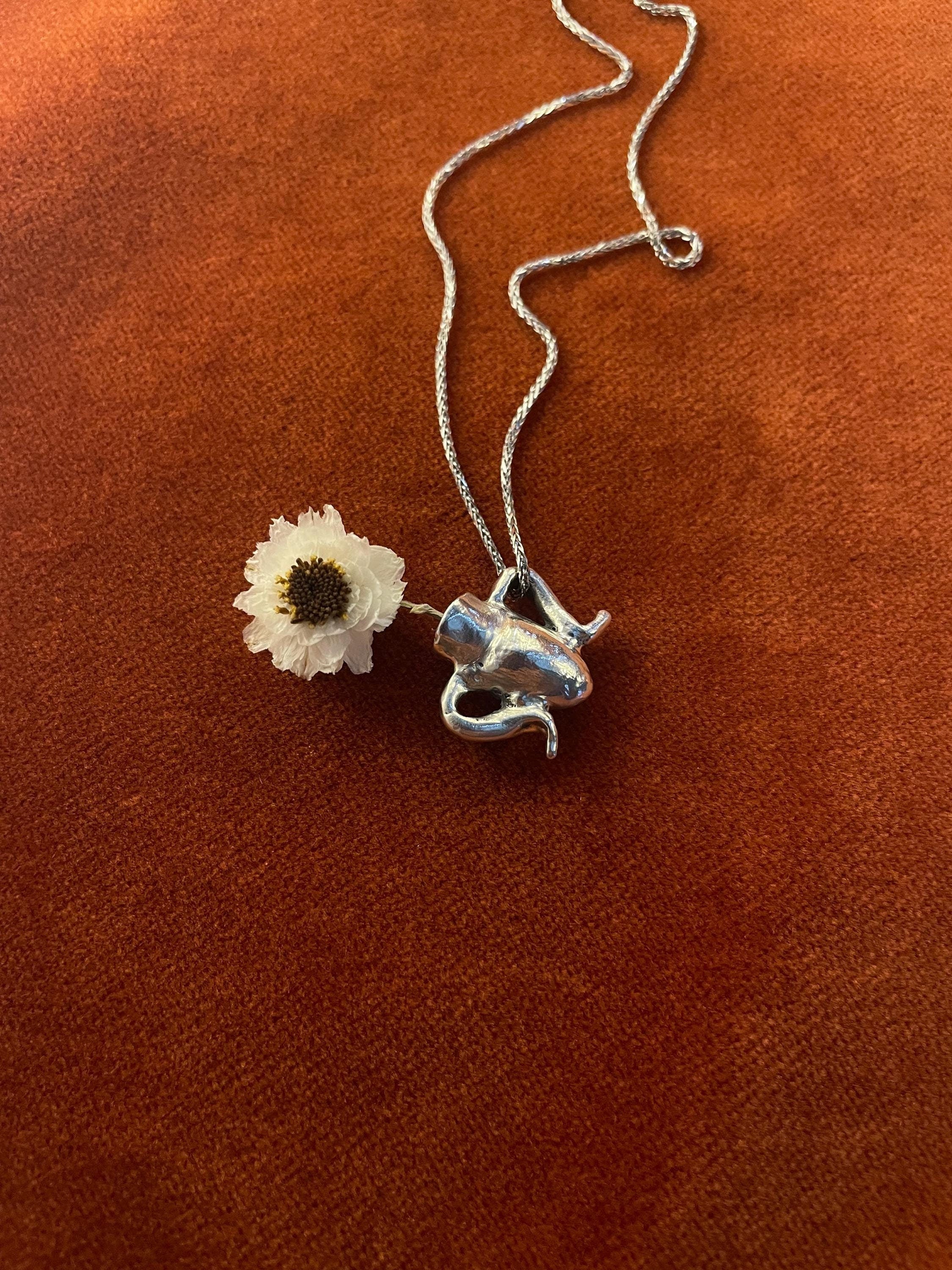 Silver chain with a white flower inside of a vase charm laying on an orange surface.