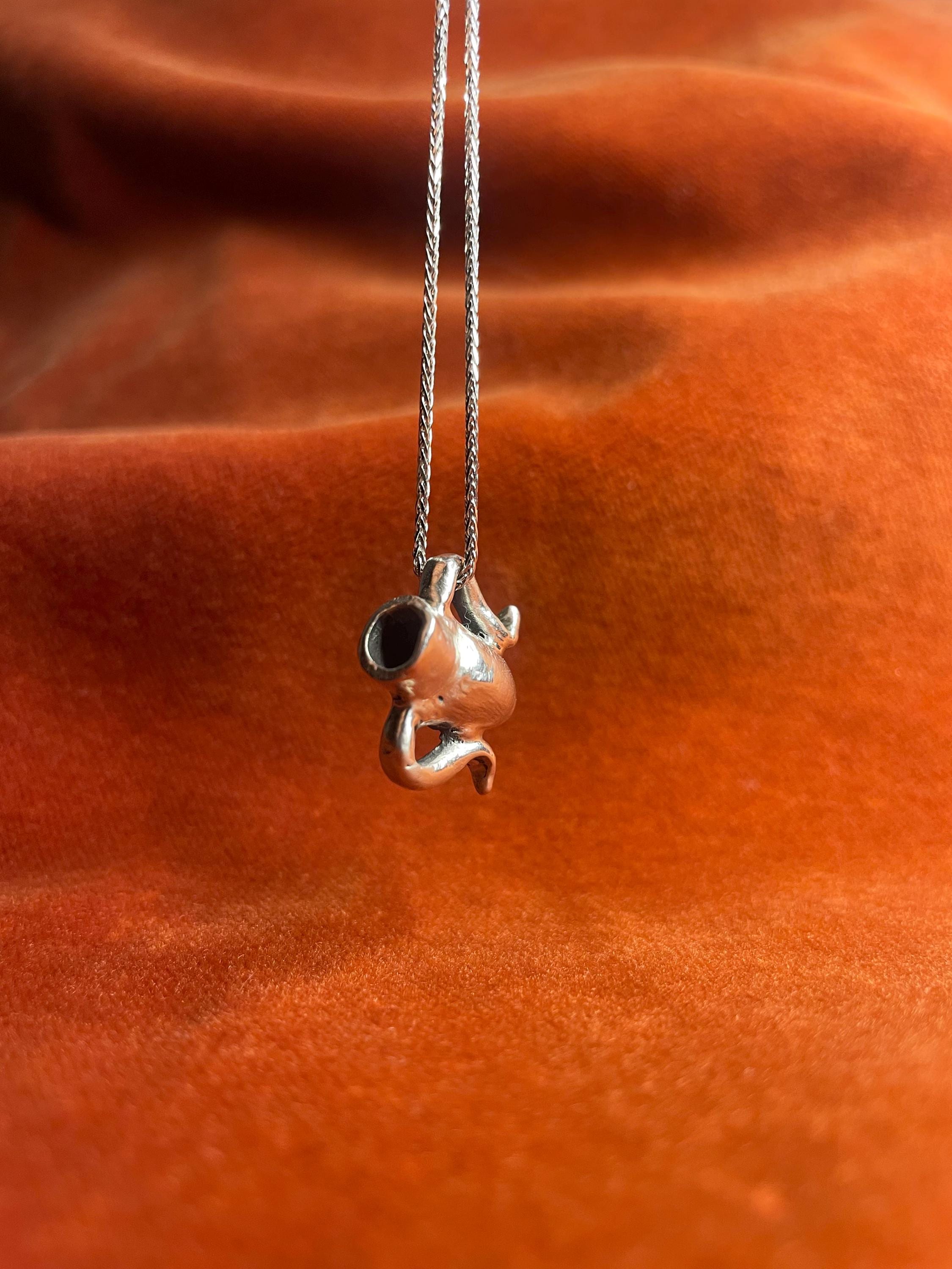 Silver chain with a small vase charm dangling above an orange fabric background.