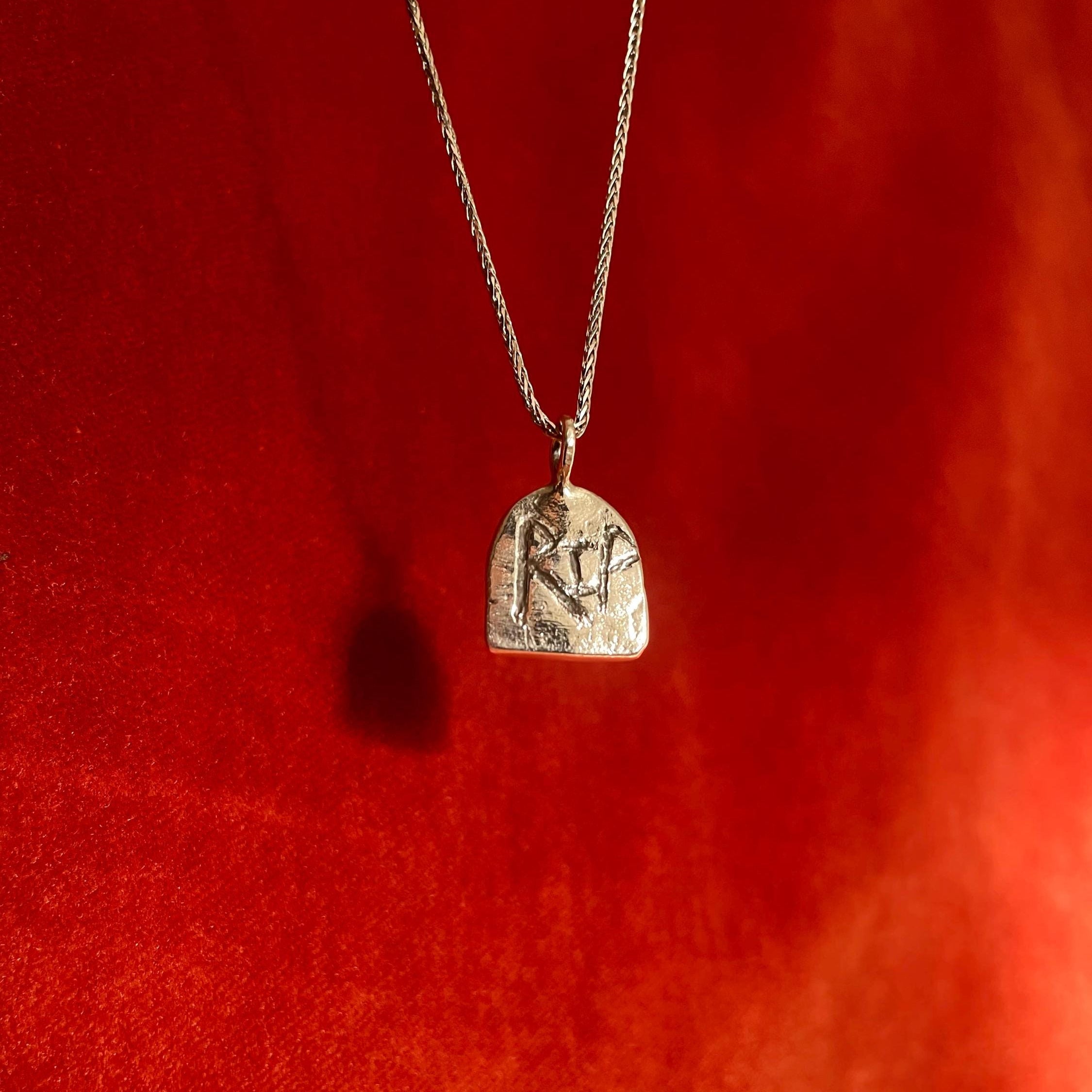 Silver necklace with RIP etched into a gravestone shaped pendant on a red background.