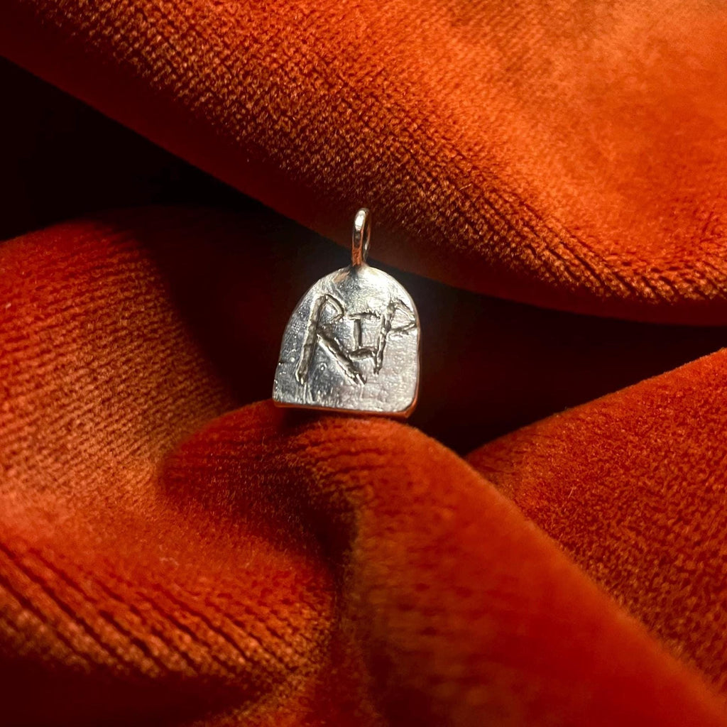 Silver pendant with engraved RIP design on a textured orange fabric background.