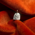Silver pendant with engraved RIP design on a textured orange fabric background.