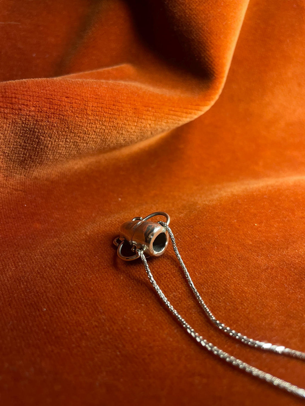 Silver chain with a vase on an orange velvet background.