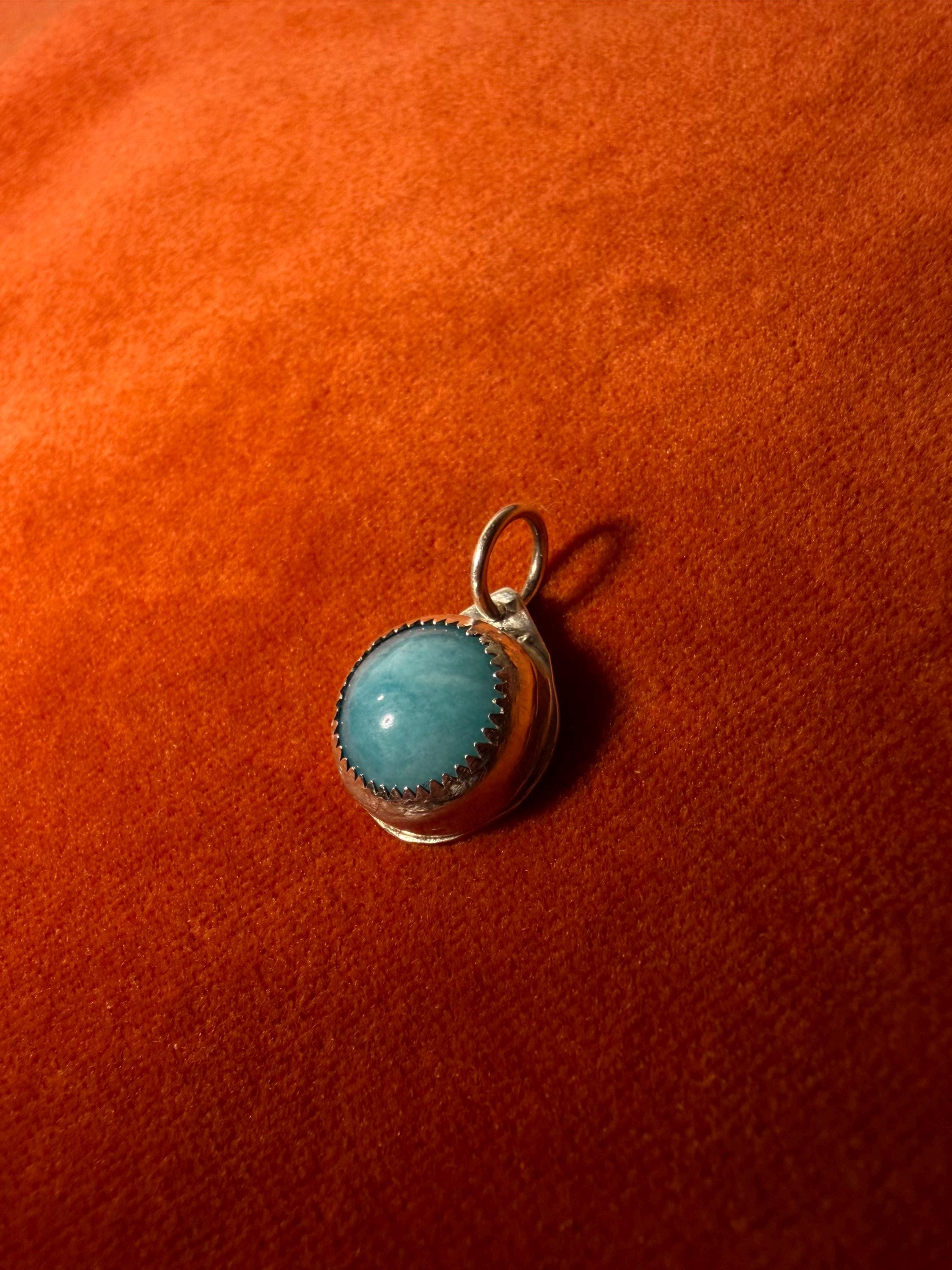 Silver pendant with a blue stone on an orange fabric background.