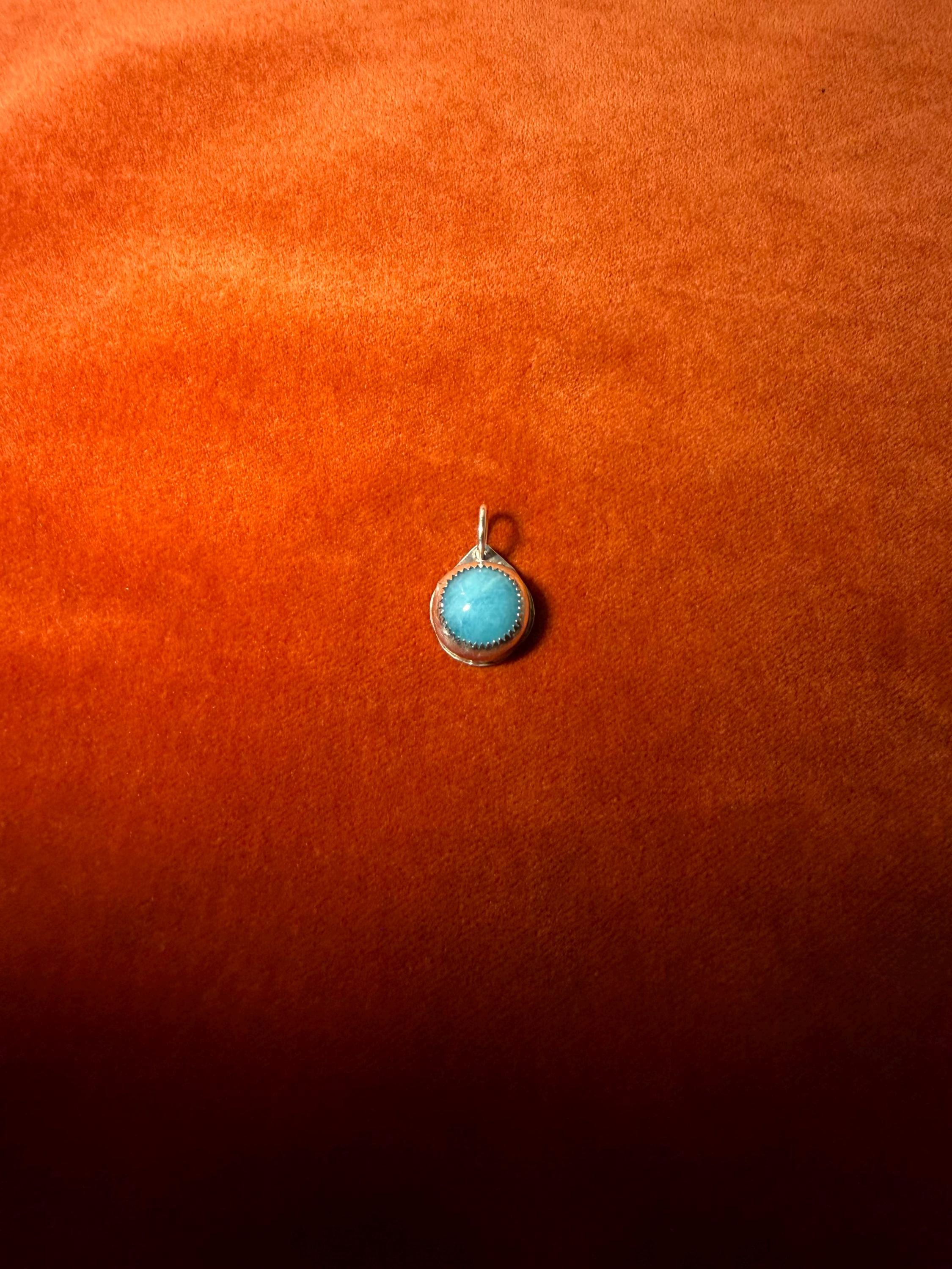 Blue-green stone pendant on an orange fabric background.