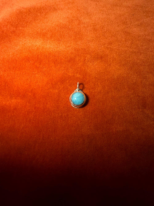 Blue-green stone pendant on an orange fabric background.