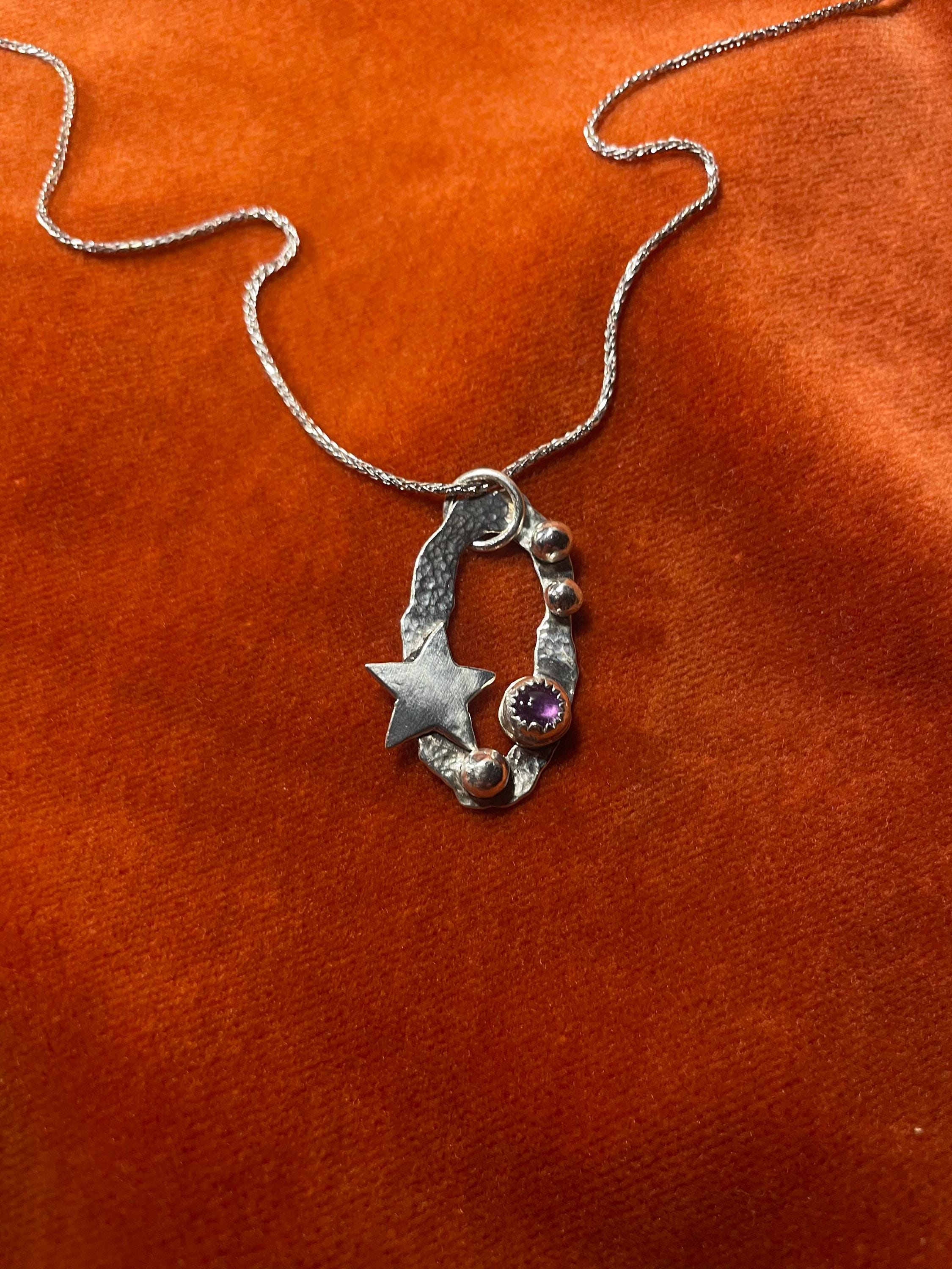 Silver chain with a celestial star charm with an amethyst stone set on an orange velvet surface.
