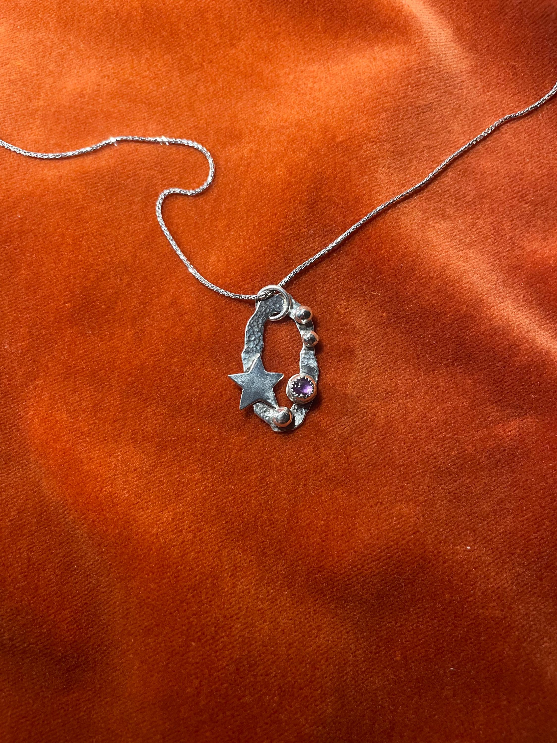 Silver chain with a star-shaped celestial charm and an amethyst stone set within on an orange velvet background.