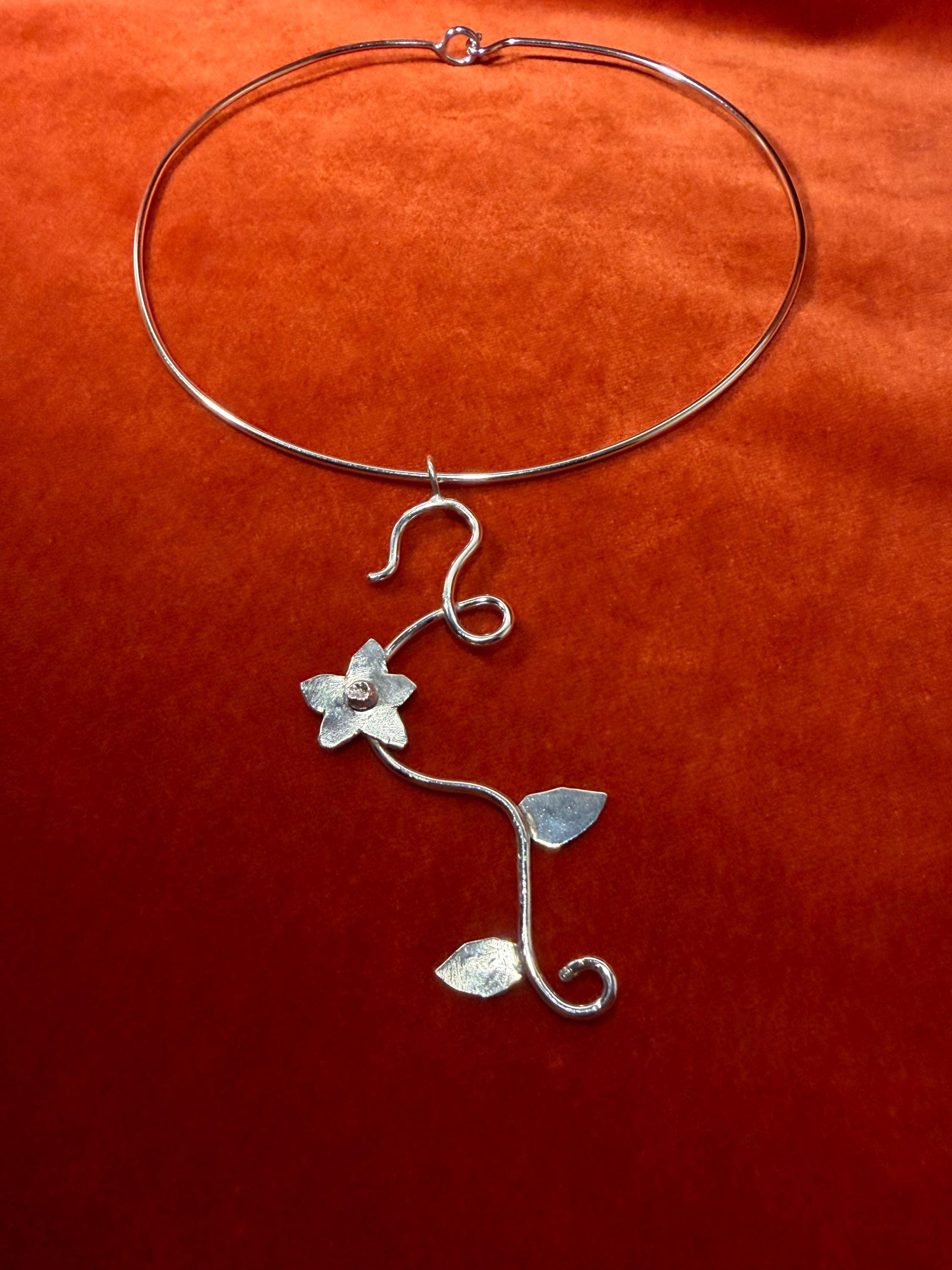 Silver choker with floral vine charm laying on a red background.