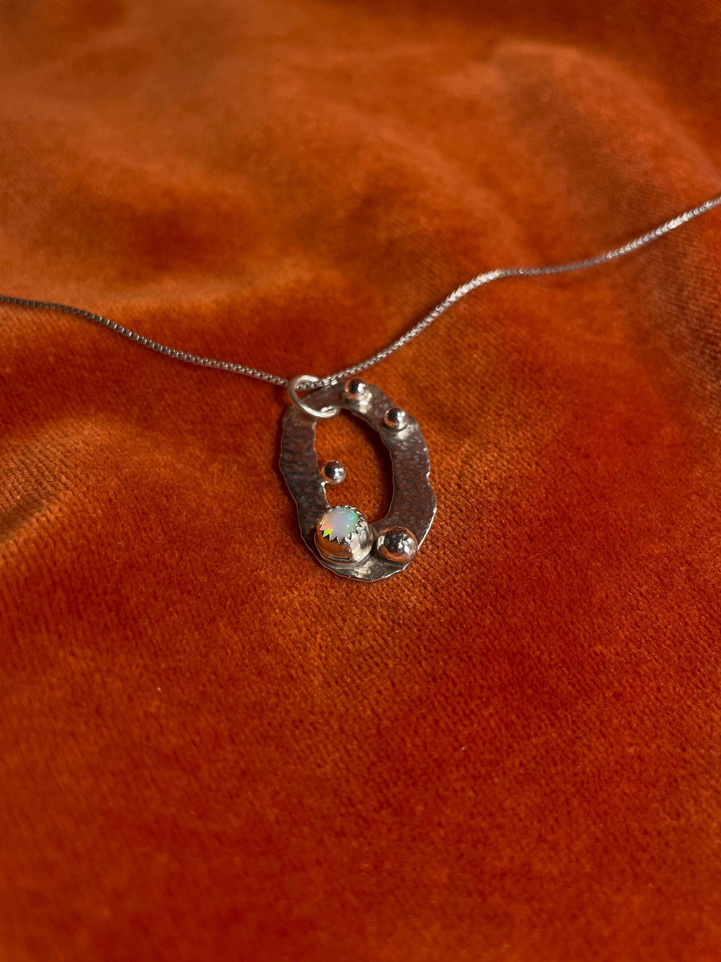 Silver necklace with an opal celestial pendant on an orange fabric background.