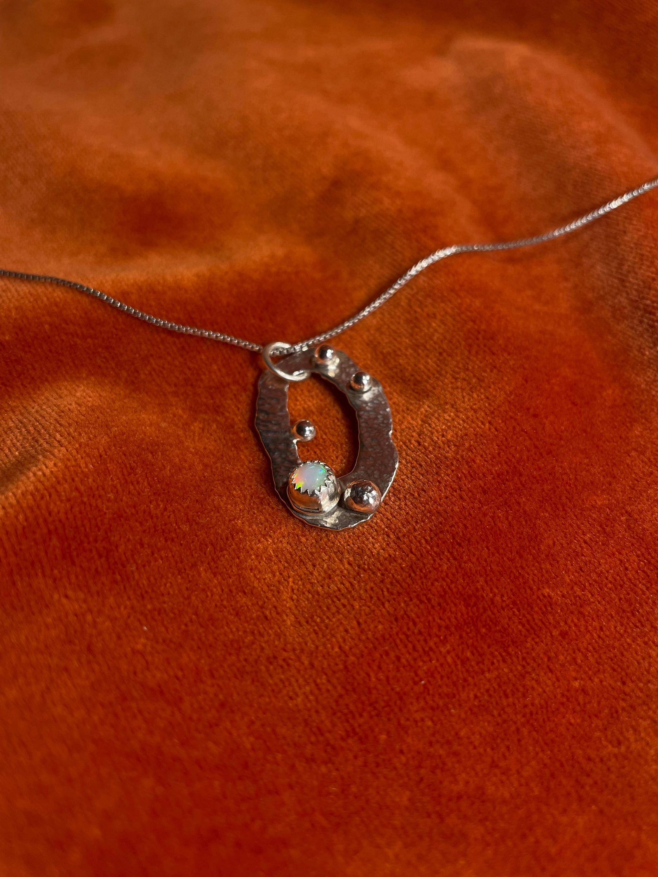 Silver necklace with an opal celestial pendant on an orange fabric background.