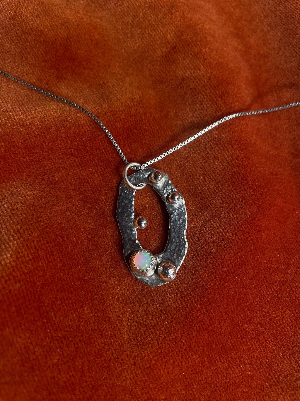 Sterling silver celestial pendant with an opal stone on a necklace laying on an orange-colored fabric background.