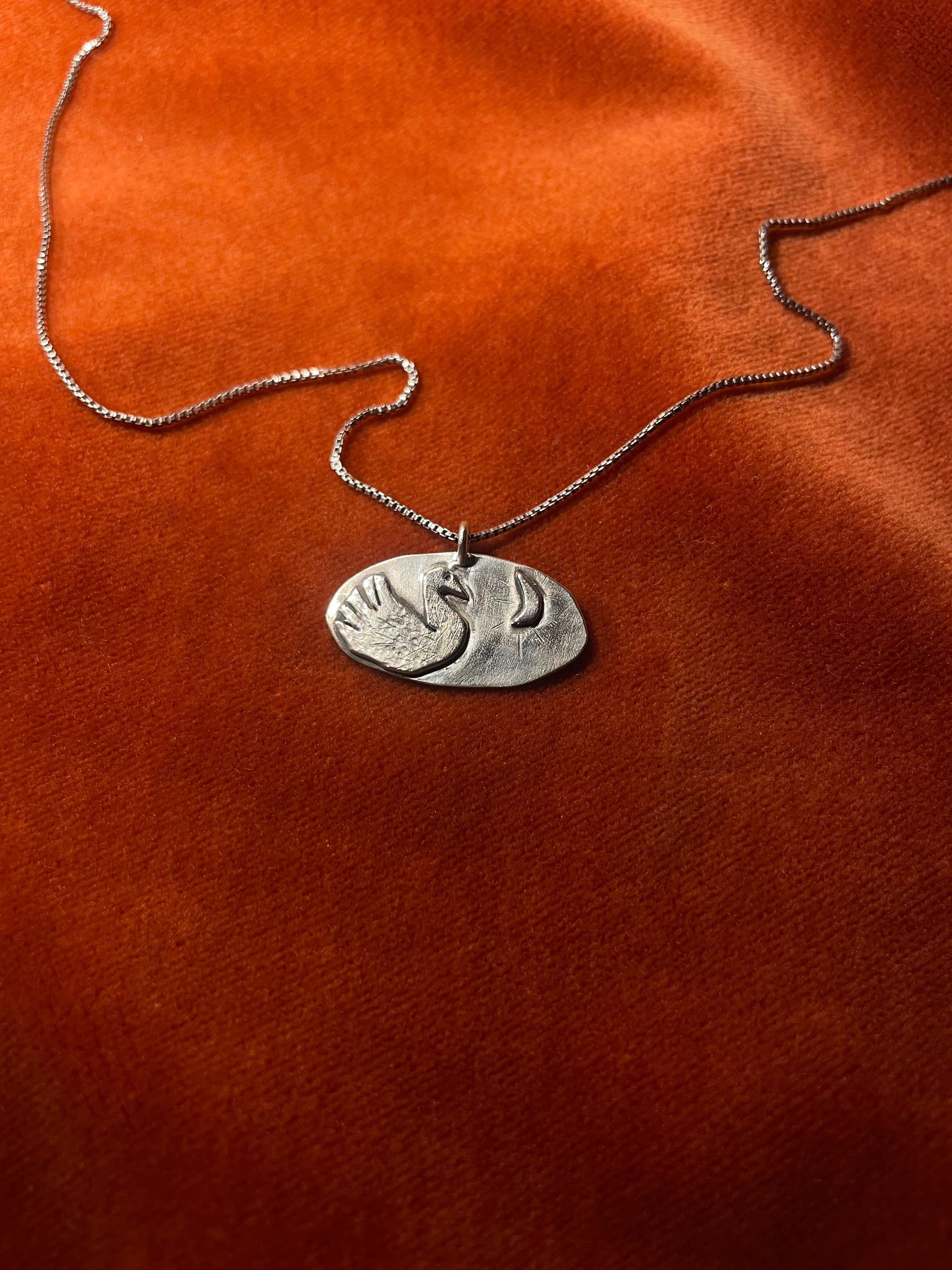 Silver chain with a swan pendant laying on an orange velvet surface.