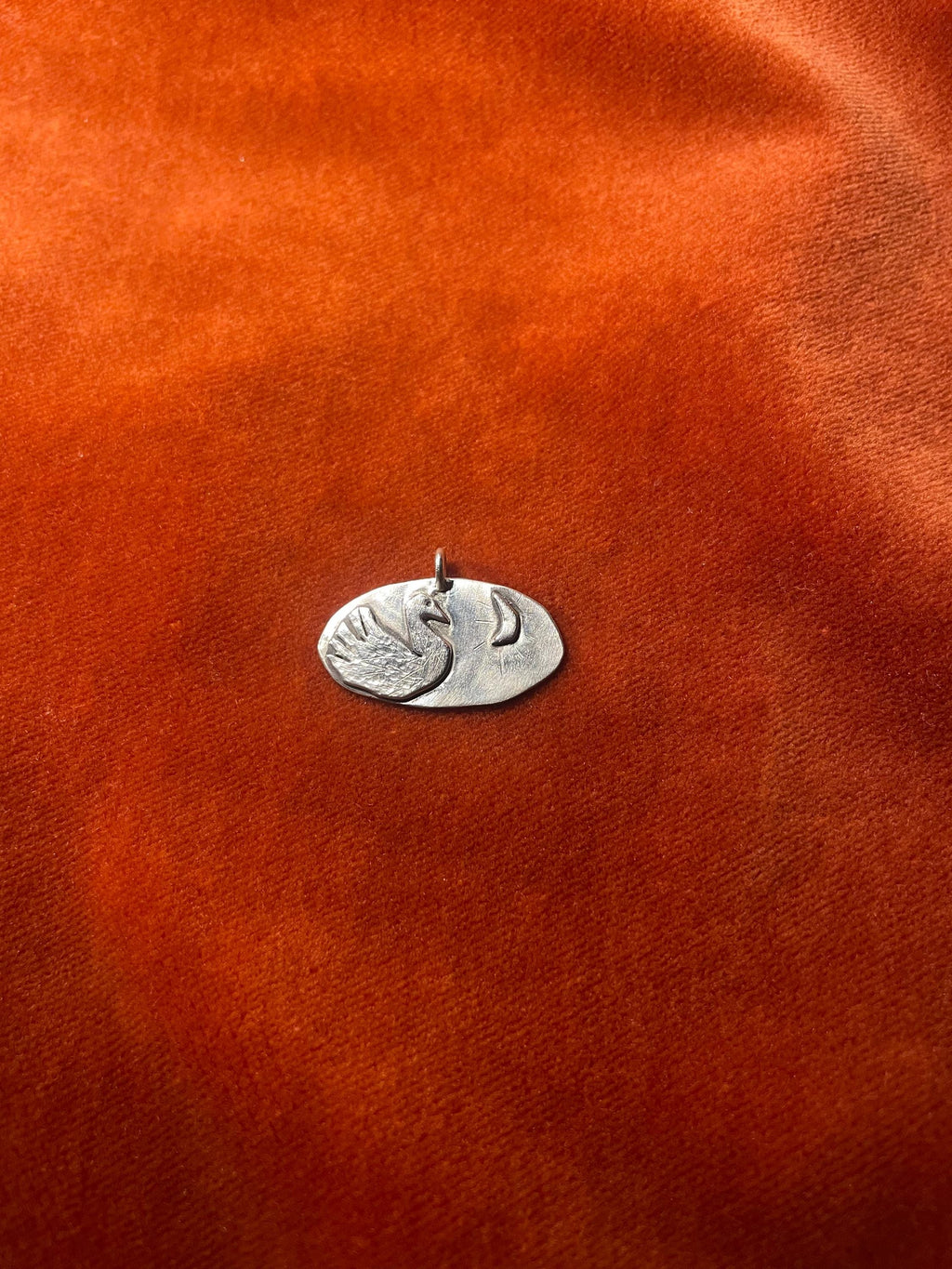 Silver swan charm on an orange velvet surface.